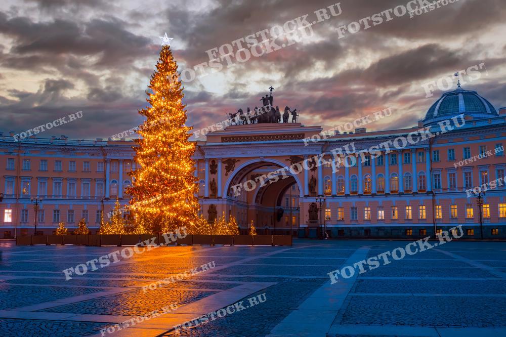 На фотографии изображена новогодняя елка, украшенная огнями, на Дворцовой площади в Санкт-Петербурге. Видны Главный штаб и Арка Главного штаба на закате. Фото может использоваться для праздничных открыток, туристических буклетов и рекламных материалов.
